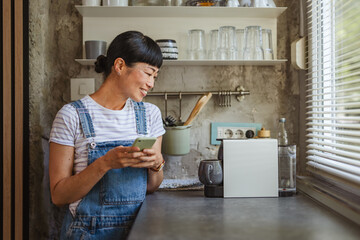 Japanese woman wait for coffee to be prepared and use mobile phone