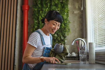 Japanese woman replies to messages while wiping dishes at home kitchen