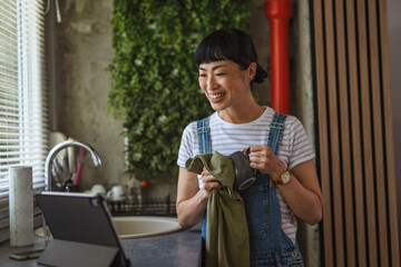 Japanese woman watch tablet while wiping dishes at home kitchen