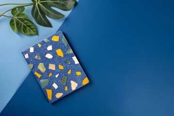 Stylish flat lay with terrazzo notebook on vibrant blue background with tropical leaves, ideal for stationery, branding or creative work scenes