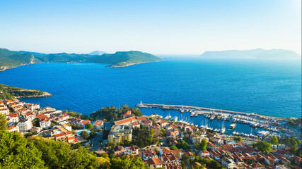 Aerial panoramic morning view of Kas, picturesque coastal town in Turkey along Mediterranean Sea. Scenic landscape shows Kas with its marina, surrounding bay, and distant islands under clear sky