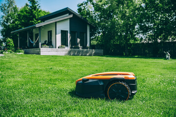 Automatic robotic lawn mower on a green lawn with cozy house in background. Grass lawn mower robot...