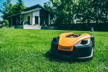 Automatic robotic lawn mower on a green lawn with cozy house in background. Grass lawn mower robot...