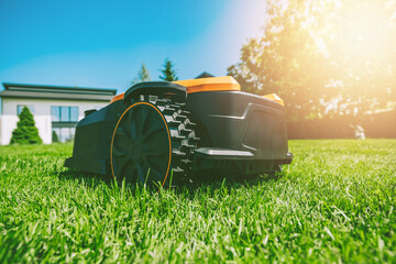 Automatic robotic lawn mower on a green lawn with modern house in background. Grass lawn mower...