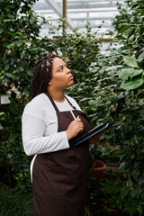 Gardening enthusiast surveys vibrant foliage in a lively greenhouse
