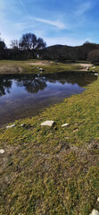 Calm lakeside view on a clear day with gentle ripples reflecting surrounding rocks and grassy shore