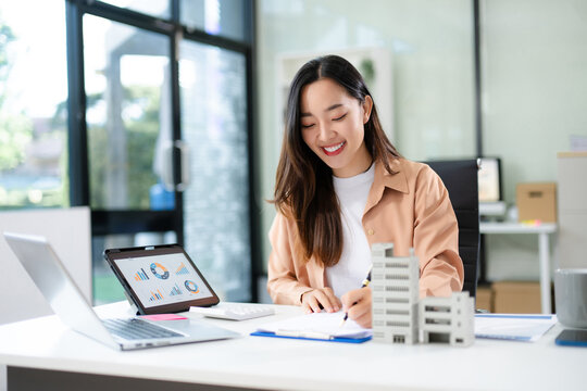 Confident Asian businesswoman smiling while presenting a modern building model in office