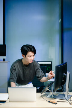 Young male programmer working with tablet and screen displaying code. Modern tech office setup, great for software, coding, IT