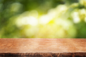 A smooth wooden tabletop set against a bright, sun-dappled green background, perfect for showcasing...