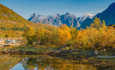 beautiful landscape of Norway with trees with yellow leaves reflecting in the water of a lake and mountain peaks in the background