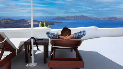 Back view of young man is laying in a blue beach chair in Summer at Oia, Santorini, Greece island