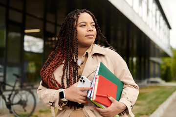University teacher carrying books and phone while enjoying a sunny day on campus