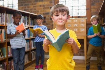 Portrait of cute boy holding book with studying with diverse students in library © vectorfusionart