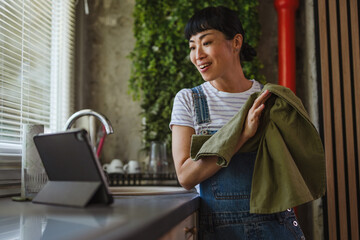 Japanese woman watch tablet while wiping dishes at home kitchen