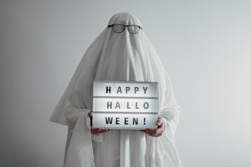 Man dressed as ghost holdsneon sign happy halloween. Festive banner