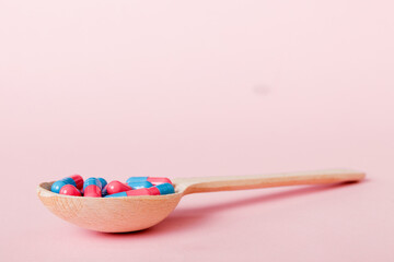 Vitamin capsules in a spoon on a colored background. Pills served as a healthy meal. Red soft gel vitamin supplement capsules on spoon