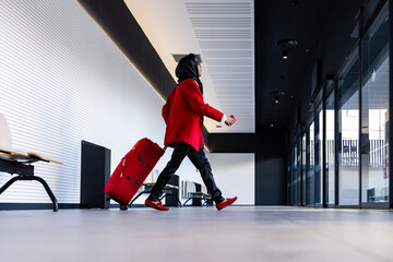 Latin businessman walking in airport terminal with red suitcase and smartphone