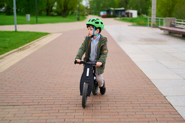 child riding balance bike in park wearing safety helmet and casual jacket. enjoying outdoor...