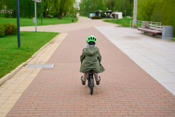 child riding bicycle on paved path in park, wearing helmet and jacket, exploring outdoors, promoting childhood adventure and balance, ideal for active lifestyle themes