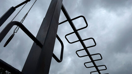 Metal monkey bars and gym rings on an outdoor playground against a dramatic cloudy sky – minimalist urban workout structure, low-angle view
