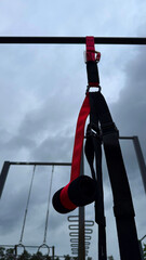 Close-up of TRX suspension training straps hanging on outdoor workout equipment under cloudy sky – calisthenics and fitness concept