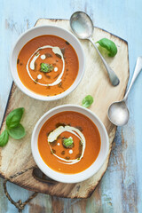 Tomato and Basil soup in two bowls on a wooden board seen from above. 