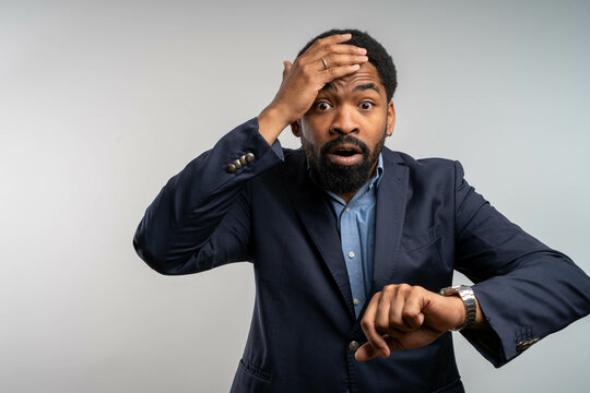 Worried African American businessman checking time on wristwatch looking at camera on white background - Powered by Adobe