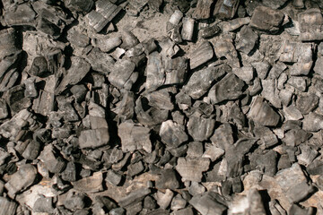 Burned charcoal pieces after barbecue grilling scattered on ground. Black and grey coal chunks with...