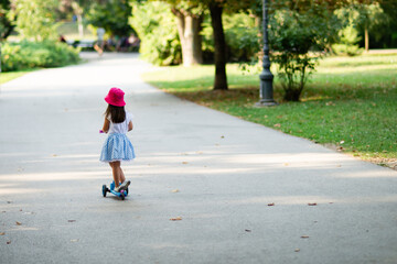 Fototapeta premium Little girl riding scooter in park during summertime