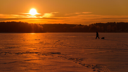 Panoramic Winter View of a Frozen Forest Lake with a Fisherman Walking Toward the Sunrise