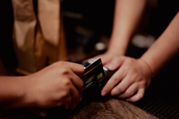 Close-up of hands using a credit card with payment terminal on wooden counter. Contactless transaction in small business setting.