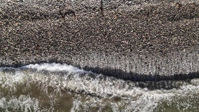 A stunning 4K aerial of San Pedro's pebble beach with waves gently crashing ashore. Ideal for nature, travel, or relaxation visuals with a peaceful, coastal vibe.