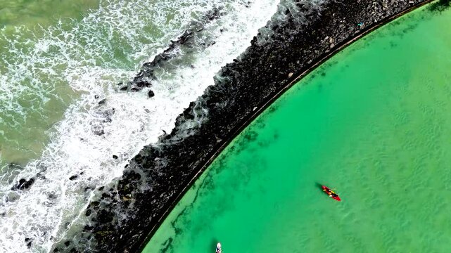 Aerial clip of canoeists in a tidal pool with the waves breaking onto rocks on the ocean side