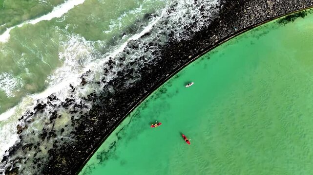 Drone clip of canoeists rowing in a tidal pool with the ocean waves crashing against the rocks in the background