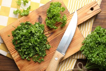 Board with cut parsley and knife on wooden table, top view