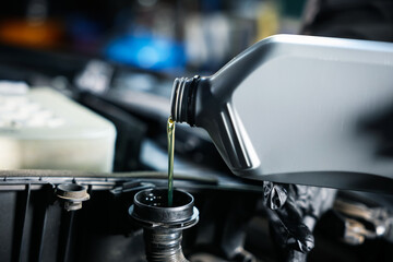 Pouring motor oil from bottle into car engine, closeup