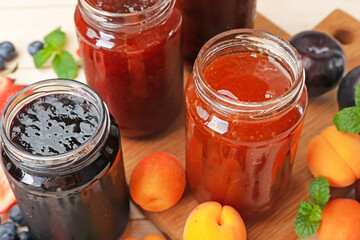 Tasty sweet jams in jars and ingredients on light table, closeup