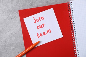 Sticky note with phrase Join Our Team, notebooks and pen on grey table, top view