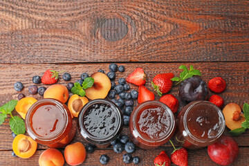 Different jams in jars and ingredients on wooden table, flat lay. Space for text