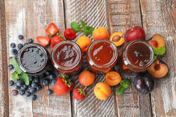 Different jams in jars and ingredients on wooden table, flat lay