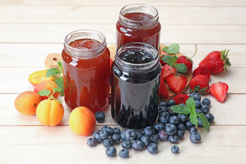 Different jams in jars and ingredients on white wooden table