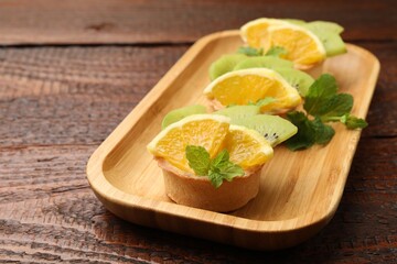 Tartlets with fruits and mint on wooden table, closeup. Delicious dessert