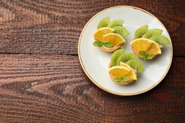 Delicious dessert. Tartlets with fruits and mint on wooden table, top view. Space for text