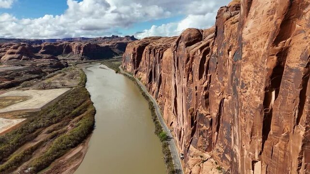 Potash Road in Moab, Utah. Close up of High Rising Red Cliffs on side of highway. Colorado River, Partly Cloudy Sky