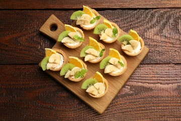 Tartlets with fruits and mint on wooden table, top view. Delicious dessert