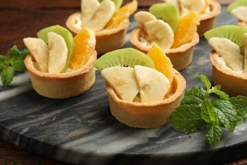 Tartlets with fruits and mint on table, closeup. Delicious dessert
