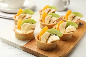 Tartlets with fruits on white marble table, closeup. Delicious dessert