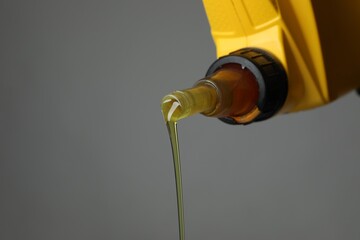 Pouring motor oil from yellow canister on grey background, closeup. Space for text