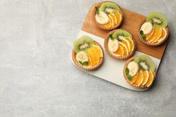 Delicious dessert. Tartlets with fruits and mint on gray textured table, top view. Space for text