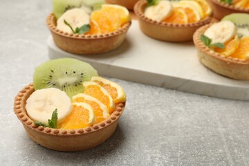 Tartlets with fruits and mint on gray textured table, closeup. Delicious dessert